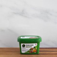 a container of salad sitting on top of a wooden table next to a white marble wall