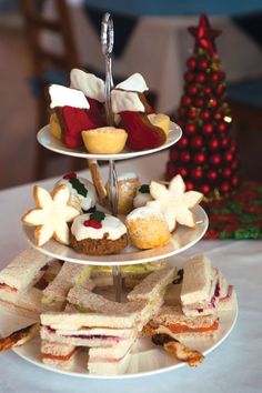 three tiered trays filled with sandwiches and pastries next to a christmas tree