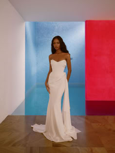 a woman in a white dress standing next to a red, blue and pink wall