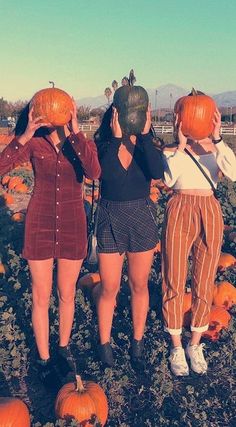 three women standing in a pumpkin patch looking at the sky