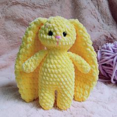 a yellow crocheted teddy bear sitting next to two balls of yarn