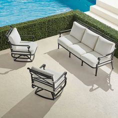 three chairs and a couch in front of a swimming pool