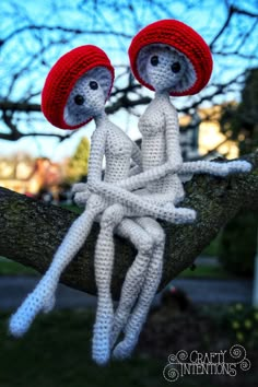 two crocheted dolls sitting on top of a tree branch with their arms around each other