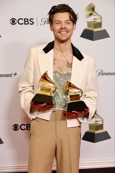 a man holding two awards in his hands and smiling at the camera while standing on a red carpet