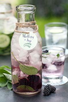 a bottle filled with ice and blackberries on top of a table next to glasses