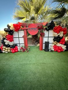 the entrance to an event decorated with red, black and white balloons in front of palm trees