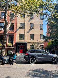 two cars are parked in front of the apartment building with red doors and large windows