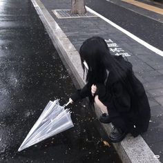 a woman kneeling down on the side of a road holding an umbrella over her head