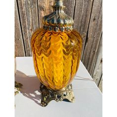 a yellow glass vase sitting on top of a table next to a wooden fence and chain