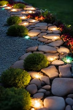 a stone path lit up with lights in the grass and flowers on either side of it