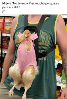 a man is holding a small dog in a pink shirt while wearing a harness on his back