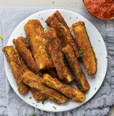 some fried food on a white plate next to a bowl of sauce and a napkin