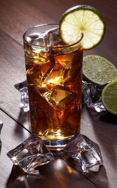 a glass filled with ice and lime on top of a wooden table