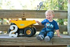 a young boy sitting on top of a wooden bench next to a yellow toy truck