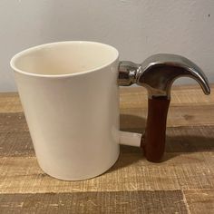 a white coffee cup with a brown handle on a wooden table next to a faucet