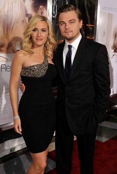 a man and woman standing next to each other in front of a poster on the wall