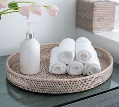 three white towels are sitting on a wicker tray next to a soap dispenser