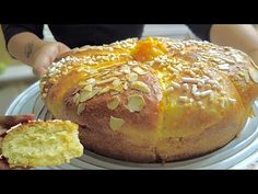 a person holding a piece of bread on top of a white plate next to a loaf of bread