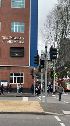 people are crossing the street in front of an university of melbourne building with traffic lights