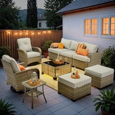 an outdoor living area with wicker furniture and lights on the side of the house