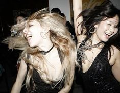 two young women are dancing together at a party, one is holding her hair in the air