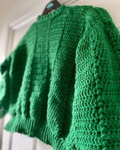 a green knitted sweater hanging from a hook on a white door frame with a pair of sunglasses in the background