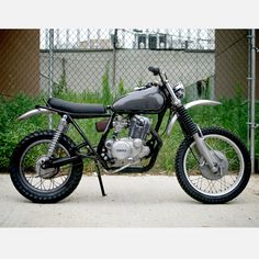 a black motorcycle parked in front of a chain link fence and green plants behind it