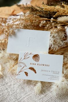 two business cards sitting on top of some dried plants