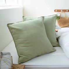 two green pillows sitting on top of a white bed next to a basket and lamp