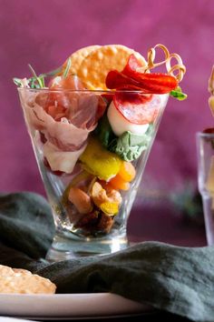 a glass filled with different types of food next to crackers and other snacks on a table