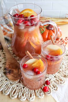 two glasses filled with liquid and fruit on top of a wooden table next to a pitcher