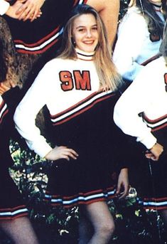 a group of young women standing next to each other wearing cheerleader outfits and holding hands behind their backs