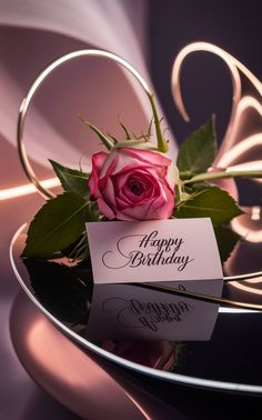 a pink rose sitting on top of a table next to a happy birthday card with writing