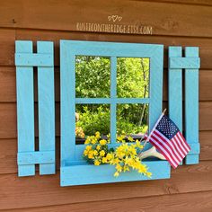 an american flag sitting in a window sill next to flowers and a potted plant