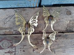 three metal butterflies are sitting on a wooden surface, one is gold and the other is brown