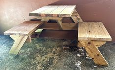 a wooden picnic table and bench in front of a pink wall