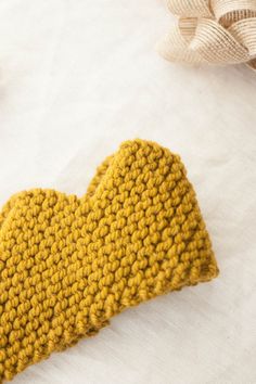 a yellow knitted mitten laying on top of a white sheet