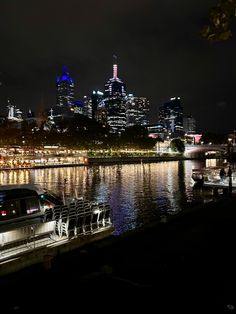 the city skyline is lit up at night as boats are docked on the riverbank