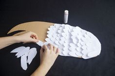 a person is cutting out white paper shapes on a black surface with a glue pen