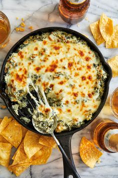 a skillet filled with spinach and cheese next to tortilla chips on a marble table