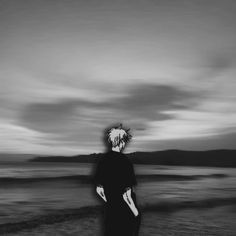 a man standing on top of a beach next to the ocean under a cloudy sky