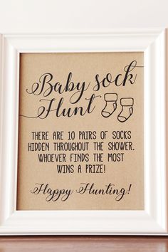 a baby sock hunt sign in a white frame on a wooden shelf next to a wall