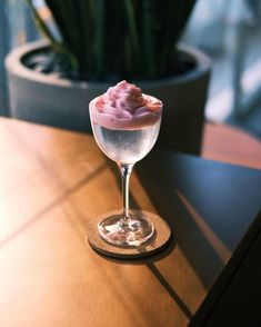 a glass filled with something on top of a wooden table next to a potted plant