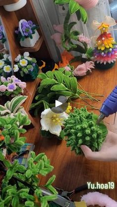 a person cutting flowers with scissors on a wooden table in front of other fake flowers