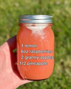 a hand holding a mason jar filled with lemon and raspberries, on top of green grass