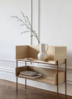 a white vase sitting on top of a wooden shelf next to a book and magazines