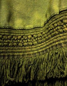 a green blanket with fringes on the top and bottom, in close up view