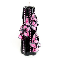 a black candle with pink and white designs on it's side, sitting in front of a white background