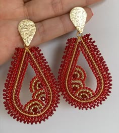 a pair of red and gold beaded earrings with an intricate design on the side