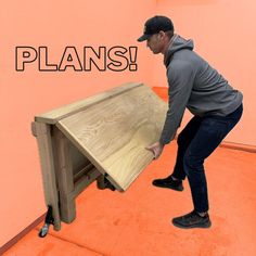 a man in grey shirt and black hat holding up a wooden table